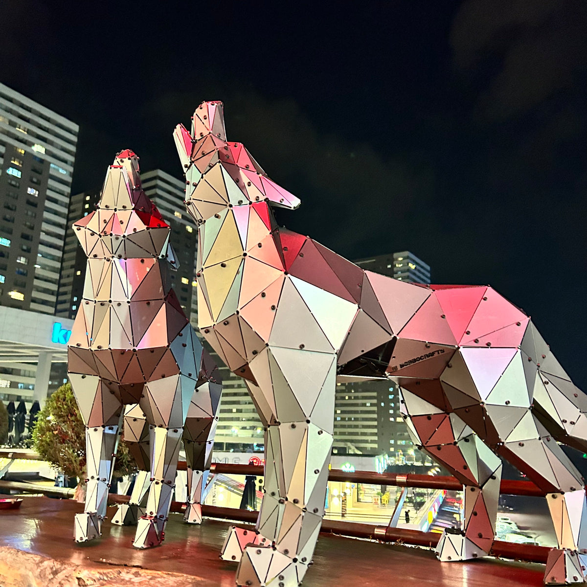 Two geometric low-poly metal wolf sculptures at night against a city skyline
