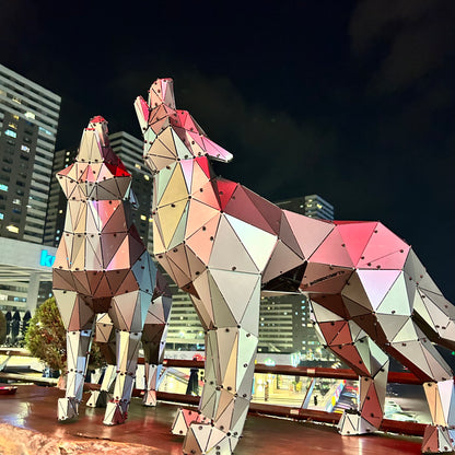 Two geometric low-poly metal wolf sculptures at night against a city skyline