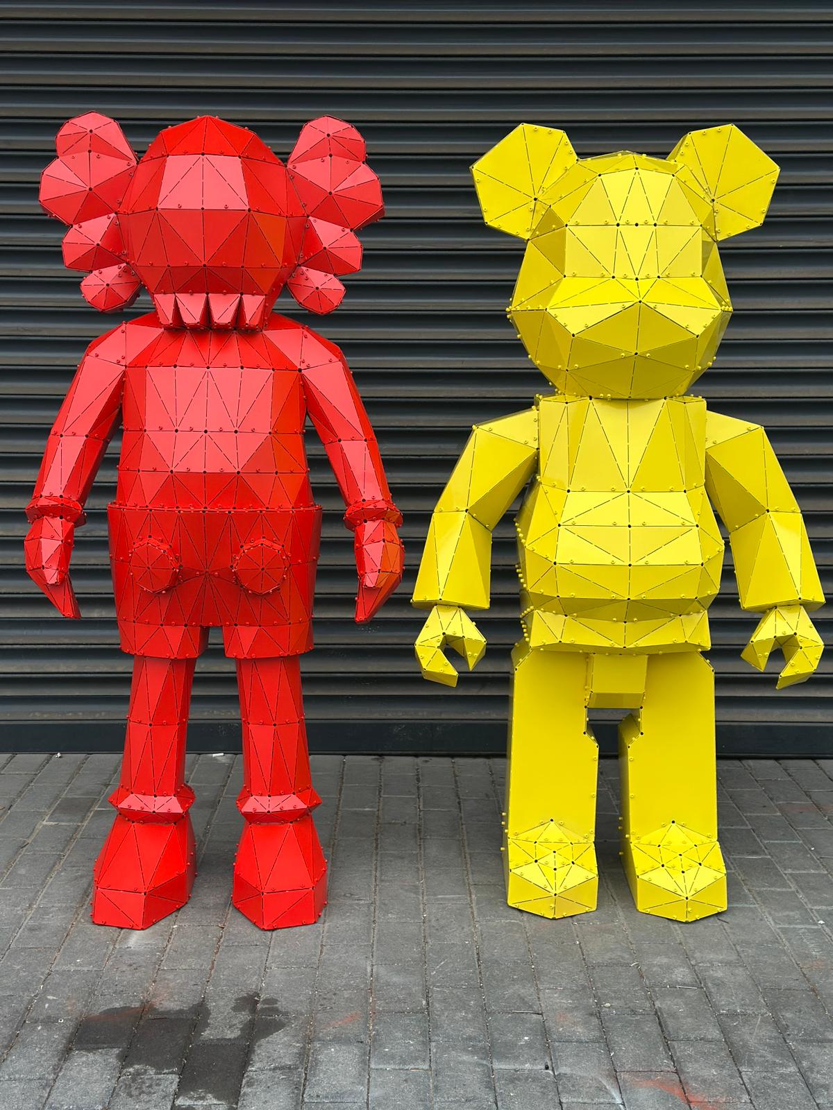 Two stylized geometric bear sculptures in red and yellow metal against a grey shutter.