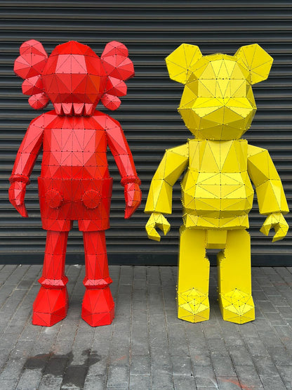 Two stylized geometric bear sculptures in red and yellow metal against a grey shutter.
