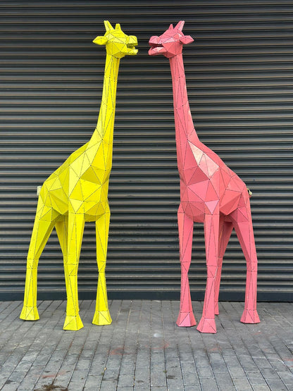 Two geometric metal giraffe sculptures in yellow and pink against a grey shutter wall.