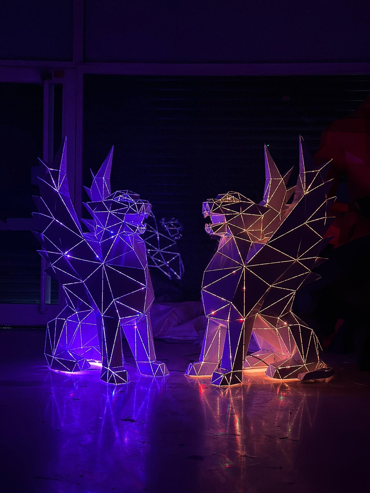 Two geometric metal sculptures of mythical creatures glowing in purple and orange neon lights.