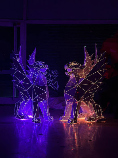 Two geometric metal sculptures of mythical creatures glowing in purple and orange neon lights.