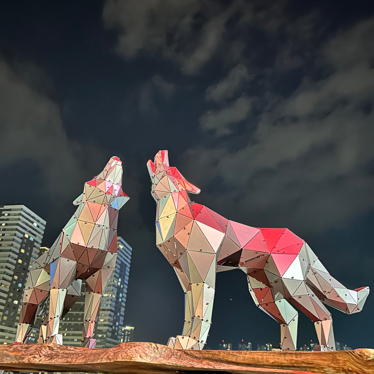 Two geometric metal wolf sculptures with iridescent colors against a night city skyline.