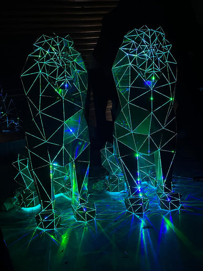 Two geometric lion sculptures made of metal with glowing green and blue LED lights.