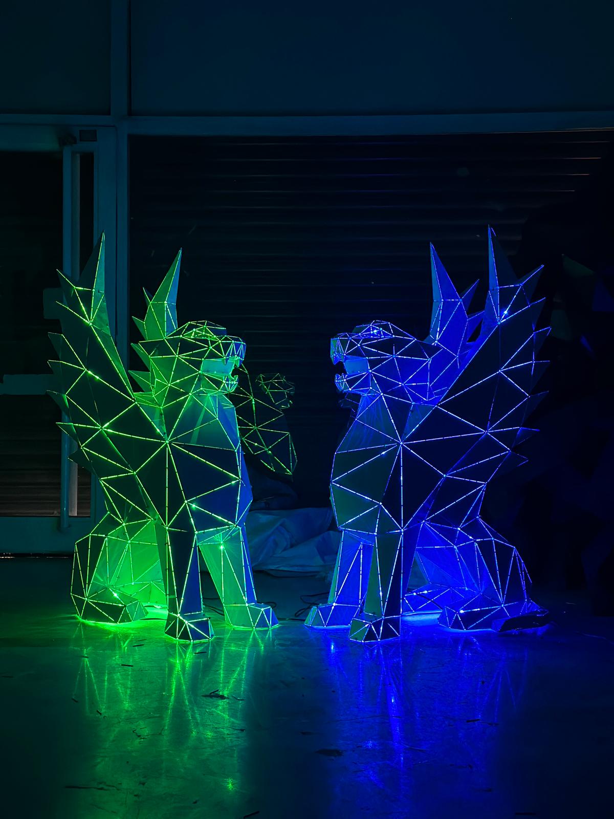 Two geometric winged griffin sculptures illuminated in green and blue LED lights