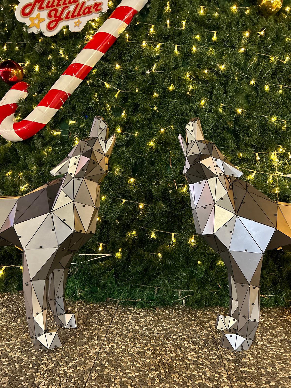 Two low-poly metal wolf sculptures facing each other in front of a decorated Christmas tree.