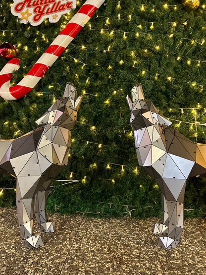 Two low-poly metal wolf sculptures facing each other in front of a decorated Christmas tree.