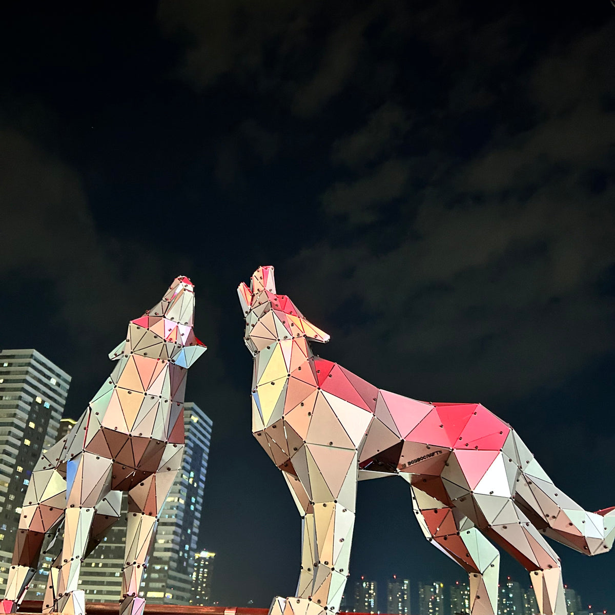 Two luxury low-poly metal wolf sculptures howling against a night city skyline.
