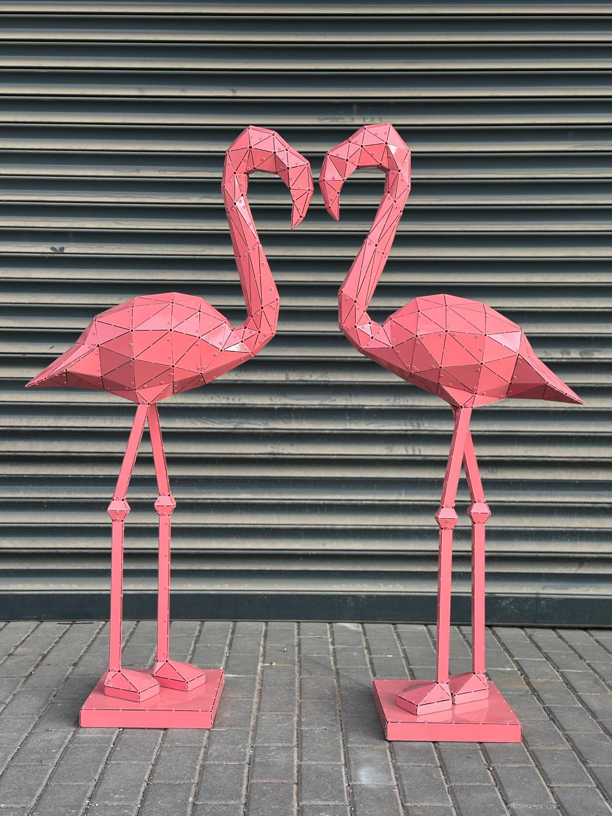 Two pink geometric metal flamingo sculptures facing each other against a grey shutter background