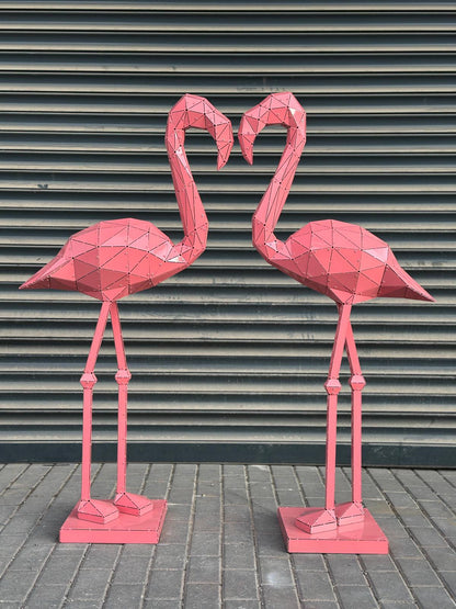 Two pink geometric metal flamingo sculptures facing each other against a grey shutter background