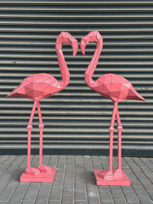Two pink geometric metal flamingo sculptures facing each other against a grey shutter background