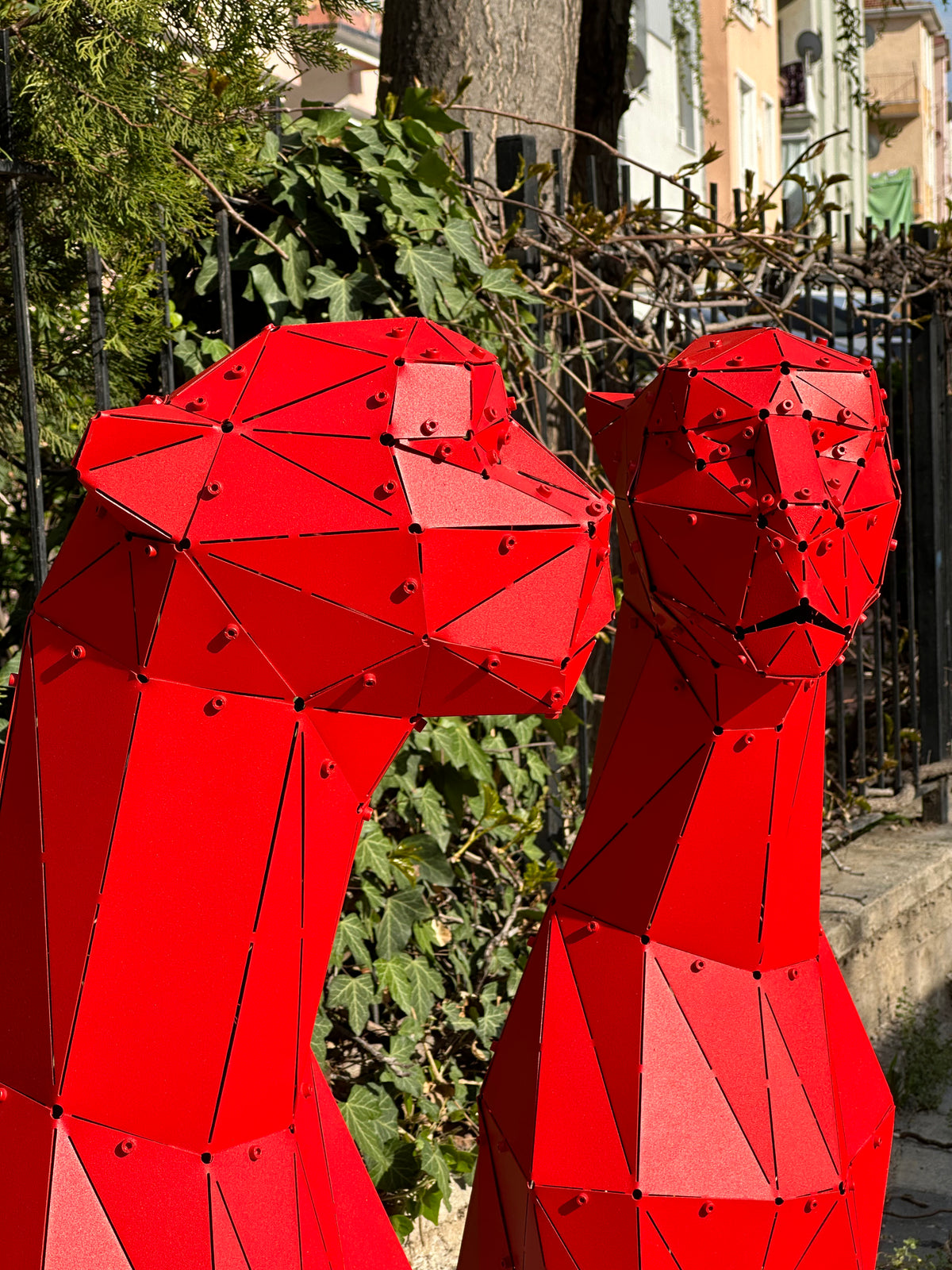 Two red low-poly metal big cat sculptures facing each other outdoors