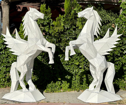 Two white geometric metal Pegasus sculptures facing each other against a green hedge.